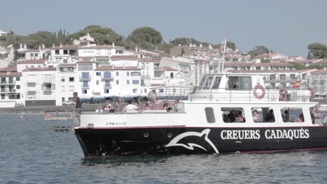 Tourists-riding-Creuers-Cadaques,-Spanish-sightseeing-boat-sailing-on-coastal-town-harbor