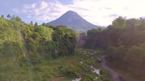 Ascending-drone-shot-of-over-natural-lake-in-nature-with-Merapi-Volcano-and-Lava-Path-and-Road-during-summer