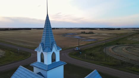 Car-parked-in-front-of-a-white-and-blue-country-church-at-sunset-in-Alberta,-Canada