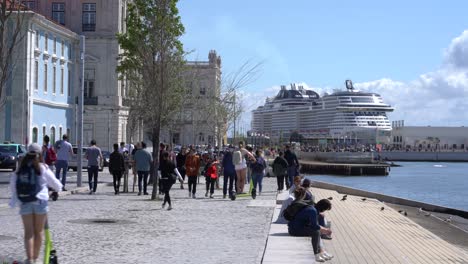 People-walking-promenade-along-Tagus-River,-Cruise-boat-moored-at-Lisbon-Cruise-Port