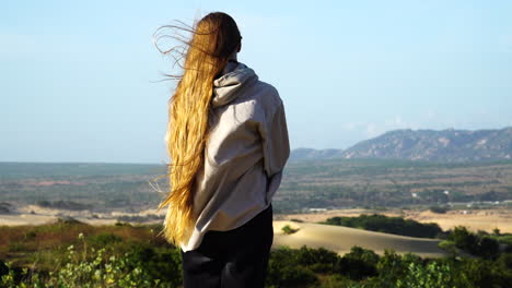 Woman-from-behind-with-blond-long-hair-and-shirt-blowing-In-the-wind-standing-at-viewpoint-of-scenic-landscape-in-Vietnam