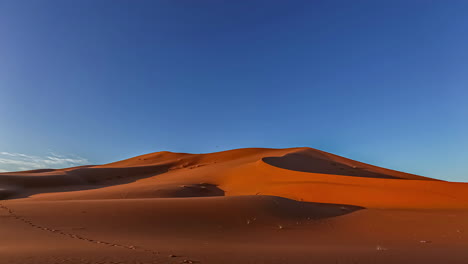 Zeitrafferaufnahme-Des-Wunderschönen-Sonnenaufgangs-über-Der-Wüste-Von-Marokko-An-Einem-Sonnigen-Tag---Sanddünen,-Die-In-Orangefarbenen-Farben-Gegen-Den-Blauen-Himmel-Leuchten