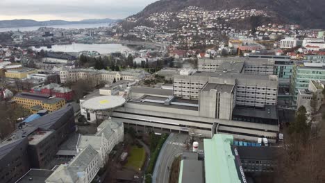Hospital-De-Haukeland-Con-La-Ciudad-De-Bergen-En-El-Fondo---Antena-En-Movimiento-Hacia-Arriba-Cerca-De-Los-Edificios-Del-Hospital-Con-Fondo-De-Paisaje-Urbano---Noruega