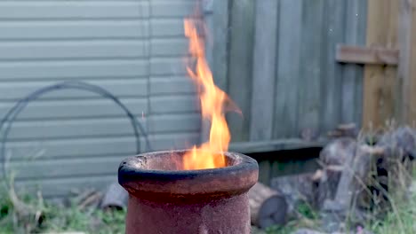 Flames-lick-up-out-the-top-of-a-terra-cotta-chimenea-during-late-evening