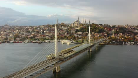 Luftdrohne-Eines-Bewölkten-Sonnenaufgangmorgens-In-Istanbul,-Türkei,-Mit-Blick-Auf-Die-Hagia-Sophia-Auf-Einem-Hügel-Und-Eine-Halic-U-Bahn-Brücke,-Während-Möwen-Vorbeifliegen-Und-Boote-Darauf-Warten,-Den-Bosporus-Zu-überqueren