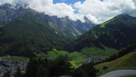 Aerial-view-while-a-drone-launch-from-a-meadow-with-a-curvy-street-and-high-mountains-in-the-background,-close-to-Vergoer---a-small-Village-in-Stubai-Valley-of-Austria