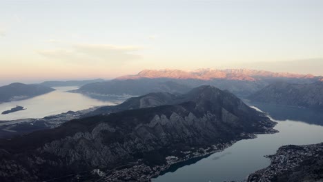 Aerial-view-of-calm-water-of-winding-bay-interrupted-by-huge-cliffs-and-mountains-during-golden-hour