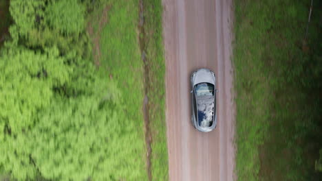 AERIAL-TOP-DOWN---A-Tesla-Model-3-drives-down-a-dirt-road-in-a-forest