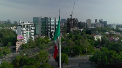 Orbital-footage-left-to-right-around-mexican-flag-with-view-of-an-principle-avenue-in-Mexico-City-at-morning