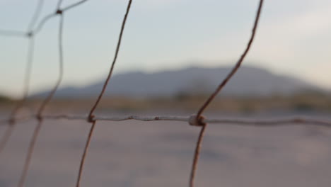 Close-up-of-a-rusty-metal-fence-along-a-field,-through-which-mountains-can-be-seen-in-the-distance