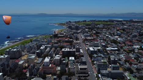 Drone-shot-of-Sea-Point,-Cape-Town---drone-is-reversing,-watching-paragliders-coming-down-from-Signal-Hill