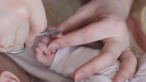 Mom's-hands-with-scissors-cutting-baby-nails-on-tiny-infant's-finger