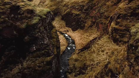 Aerial-view-of-a-stream-of-water-flowing-in-a-cliffy-gorge-in-Iceland,-during-winter-time