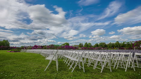 Rows-of-wooden-folding-white-chairs-standing-on-the-garden-floor-with-green-grass-with-white-clouds-passing-by-at-daytime-in-timeplase