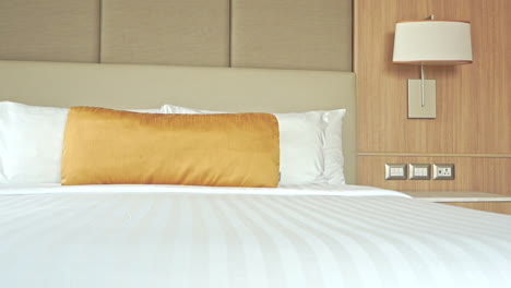 Close-up-pan-across-a-large-comfortable-hotel-bed-decorated-with-a-gold-throw-pillow