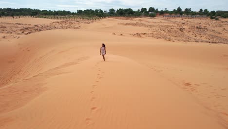 aerial-tracking-backwards-of-woman-walking-top-of-desert-sand-dunes-in-Mui-Ne-Vietnam