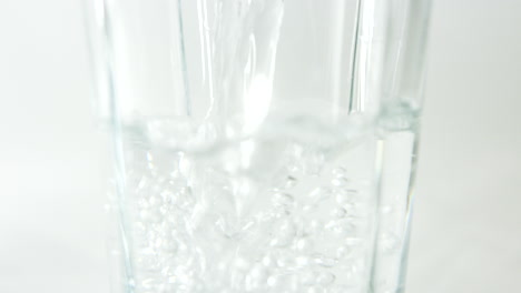 Close-up-slow-motion-footage-of-centre-of-glass-being-filled-with-water-against-clean-light-background