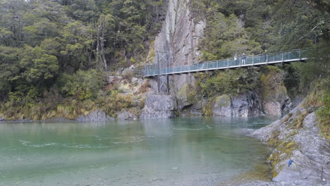 People-walking-across-bridge-in-a-lush-green-lake-in-New-Zealand