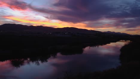 Schwenk-Eines-Atemberaubenden-Sonnenuntergangs-Mit-Brillanten-Farben,-Die-Von-Einem-Ruhigen-Fluss-Reflektiert-Werden