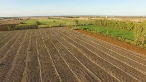 Wide-view-of-the-beautiful-flat-farmland-of-Canada-as-a-tractor-works-in-a-dusty-brown-field