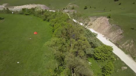 Aerial-view-of-wide-open-green-meadow-with-a-small-orange-tent