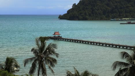 A-pier-with-a-small-red-roof-at-the-end,-in-the-ocean-with-palm-trees