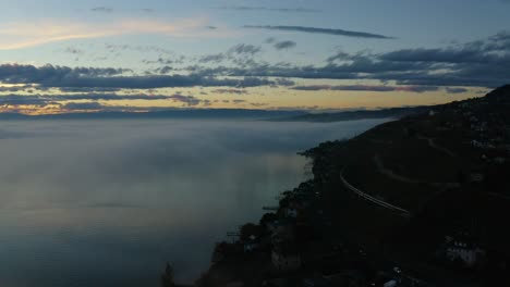 Overflying-shore-of-Lake-Léman-with-Swiss-train-passing-along-and-disappearing-in-the-fog-at-sunset