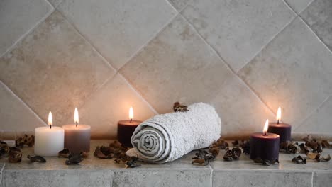 relaxing-spa-background-with-candles-with-flickering-flames,-some-wooden-petals-and-a-towel