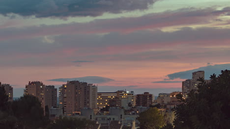 Slow-zoom-timelapse-of-red-and-pink-clouds-moving-fast-during-sunset-over-a-view-of-apartment-buildings-and-hotels-in-Costa-Del-Sol,-Spain