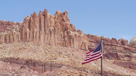 Slow-motion-shot-of-American-flag-waving-in-the-wind-in-front-of-huge-rocks-in-Capitol-Reef-National-Park-in-Utah,-USA