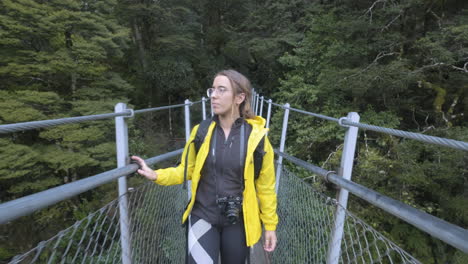 Girl-in-yellow-jacket-with-camera-walking-along-bridge-in-New-Zealand