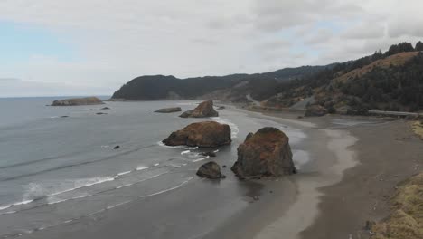 Verträumte-Luftaufnahme-Der-Küste-Von-Oregon-Mit-Großen-Felsvorsprüngen-Und-Wellen,-Die-An-Einen-Natürlichen-Strand-Schlagen
