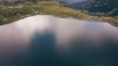 Wide-aerial-drone-slowly-flying-over-a-lake-looking-down-onto-a-valley-a-mountain-range