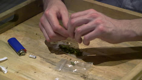 a-man-topping-his-tobacco-with-a-lot-of-marijuana-on-a-wooden-tray-at-his-home