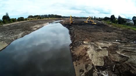 Three-Yellow-Excavators-are-working-with-Buckets-to-Clear-Mud-Sludge-and-Debris-from-the-Bottom-of-the-Drained-River