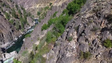 Descending-aerial-view-of-steep-canyon-walls-with-a-white-water-river-flowing-below