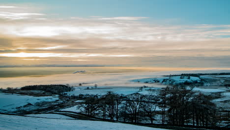 Cloud-inversion-covering-the-Eden-Valley-in-Cumbria-with-the-Lakeland-mountains-in-the-background,-and-the-sun-breaking-through-the-clouds-and-lighting-up-the-foreground