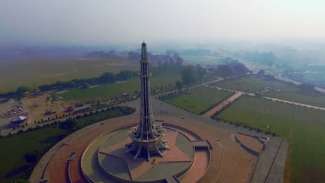 Aerial-rotating-view-of-Minar-e-Pakistan-against-the-sun,-A-national-monument-located-in-Lahore,-Pakistan