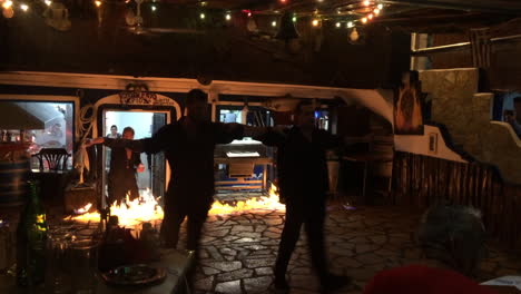 Two-waiters-dancing-traditional-greek-dance-in-front-of-fire-in-local-greek-pub
