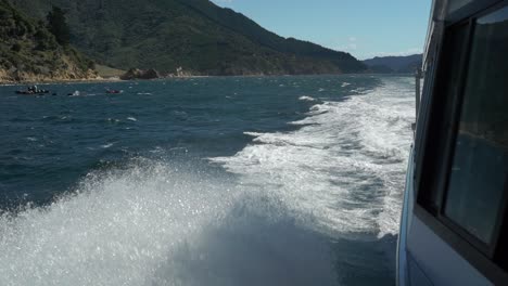 SLOWMO---Foamy-waves-breaking-on-side-of-cruise-boat-in-Marlborough-Sounds,-New-Zealand-with-green-hills-in-background