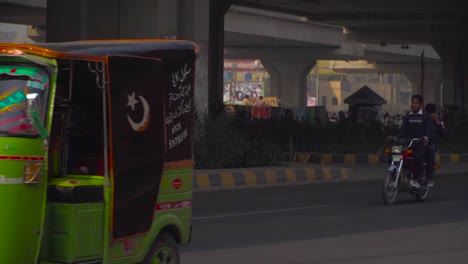 Rickshaw`s-close-up-at-the-road-under-the-fly-over,-passing-motor-bikes-and-cars,-cycle,-Buses