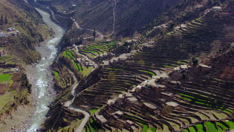 Aerial-view-of-The-river-of-the-Kashmir-with-simple-lifestyle-of-Kashmir,-calls-for-simple-houses,-with-wood-borders,-thatched-roofs-and-small-cottages,-A-curvy-road-with-river-making-beautiful-view
