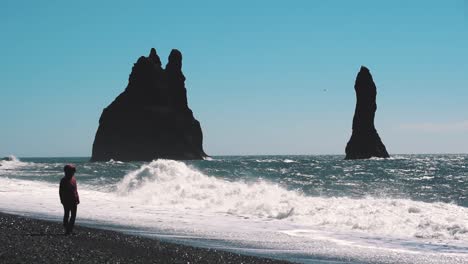 Silhouette-facing-the-ocean-as-big,-slow-motion-waves-hit-the-black-sand-beach-at-Reynisfjara