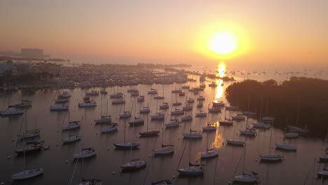 Aerial-fly-over-boat-filled-harbor-and-sunrise