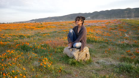 A-gorgeous-young-girl-crying-and-looking-depressed-and-sad-sitting-alone-in-a-meadow-of-wild-flowers-with-wind-blowing-her-hair-at-sunset-SLOW-MOTION