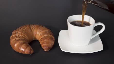 Pouring-french-press-coffee-into-white-cup-next-to-a-croissant