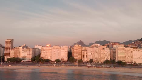 Aerial-panorama-showing-the-total-beach-neighbourhood-of-Copacabana-in-Rio-de-Janeiro-with-the-high-rise-buildings,-favelas,-Sugarloaf-mountain-and-oil-rig-in-front-at-golden-hour-sunrise