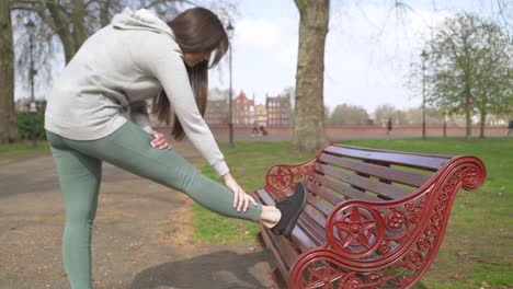 Female-jogger-stretching-her-leg-on-a-Park-bench-before-run