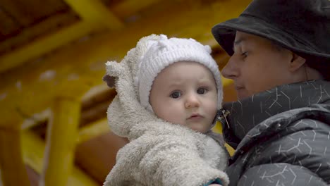 Young-mother-holding-baby-boy-in-a-cute-wite-clothing-outdoors-on-a-cold-winter-day