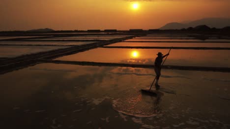 Worker-doing-overtime-in-the-golden-evening-light-silhouetted-racking-the-salt-field-for-harvest-in-slow-motion